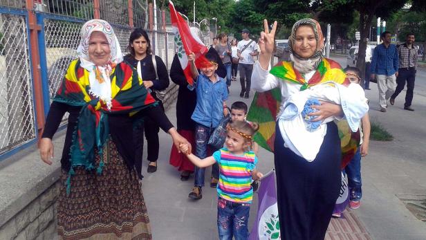 Eine Gruppe von Frauen und Kindern demonstriert mit kurdischen Flaggen auf einer Straße.