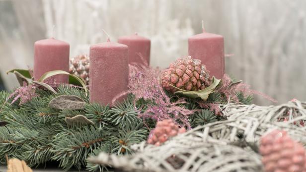 Ein Adventskranz mit vier rosa Kerzen, Tannenzweigen und glitzernden Dekorationen.