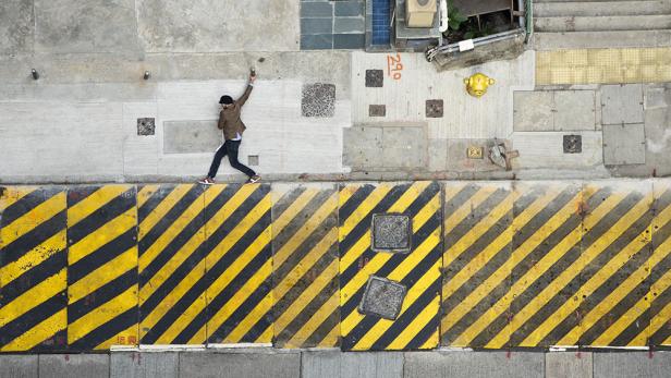 Ein Mann balanciert auf einer gelb-schwarz gestreiften Begrenzung auf einer städtischen Fläche.