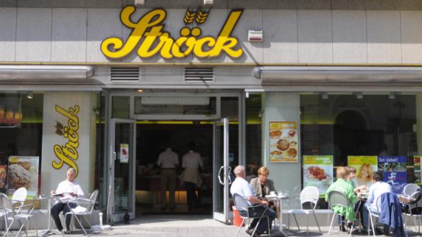 Menschen sitzen vor einer Ströck-Filiale an Tischen.