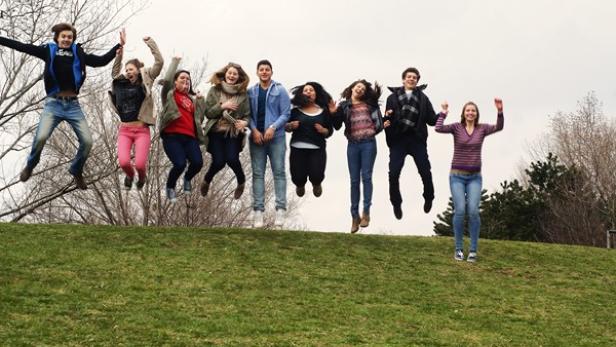 Eine Gruppe junger Leute springt auf einem Hügel in die Luft.