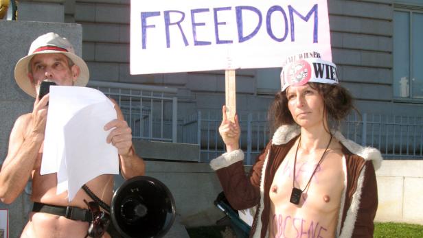 Zwei Demonstranten, einer mit einem Schild „Freedom“, protestieren halbnackt.