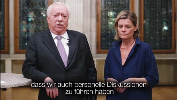 Ein Mann im Anzug und eine Frau in einem blauen Hemd stehen nebeneinander.