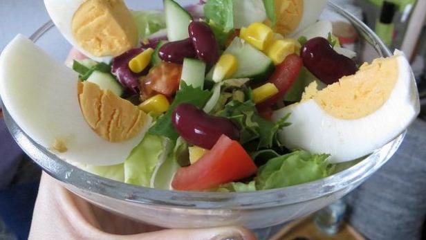 Ein gemischter Salat mit Ei, Bohnen, Mais und Tomaten in einer Glasschüssel.