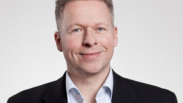 Ein Mann mit kurzem, grauem Haar und einem dunklen Anzug lächelt.