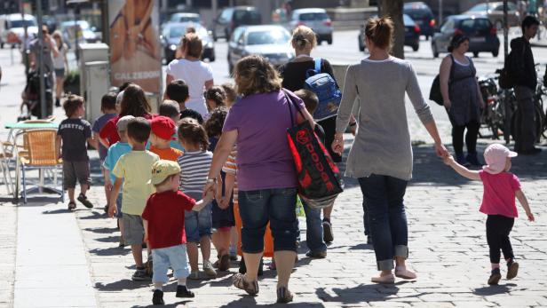 Eine Gruppe von Kindern geht an der Hand von Erwachsenen eine Straße entlang.