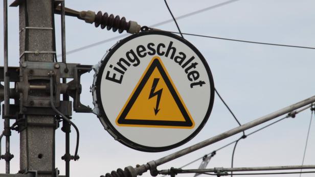 Ein Warnschild mit der Aufschrift „Eingeschaltet“ und einem Blitzsymbol an einem Strommast.