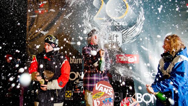 Snowboarder feiern mit Champagner auf dem Podium eines Wettbewerbs.