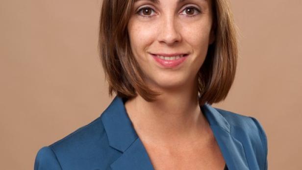 Eine Frau mit braunen Haaren und blauem Blazer lächelt in die Kamera.