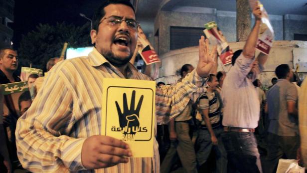 Ein Mann hält ein Schild mit einer schwarzen Hand und dem Wort „Rabia“ auf einer Demonstration.