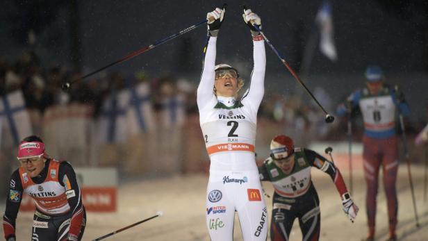 Eine Skilangläuferin jubelt mit erhobenen Armen im Ziel.