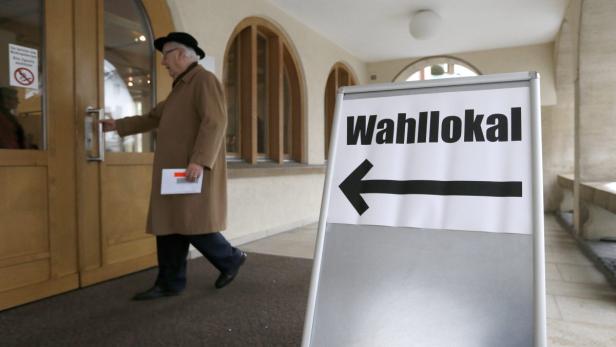 Ein älterer Mann betritt ein Wahllokal, auf das ein Schild mit der Aufschrift „Wahllokal“ hinweist.