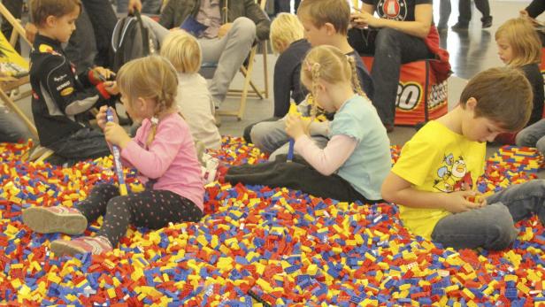 Eine Gruppe von Kindern sitzt in einem Becken voller bunter Legosteine und spielt.