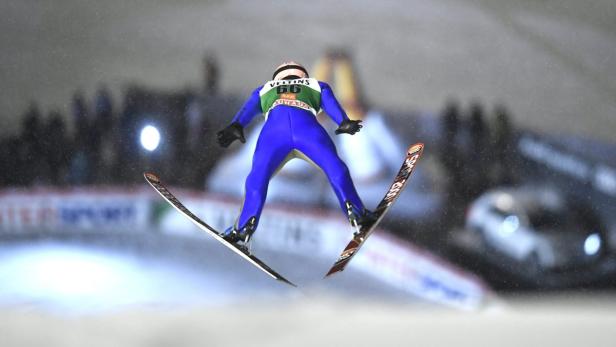 Ein Skispringer in blauer Kleidung während eines Sprungs.