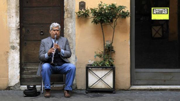 A man plays a clarinet next to a shop with a sign A man plays a clarinet next to a shop with a sign that reads "For rent" in downtown Rome November 10, 2011. Political and economic crisis in Italy spurred fears of a split in the euro zone with borrowing costs for Europe's third biggest economy at unsustainable levels and the bloc unable to afford a bailout. REUTERS/Stefano Rellandini (ITALY - Tags: POLITICS BUSINESS SOCIETY)