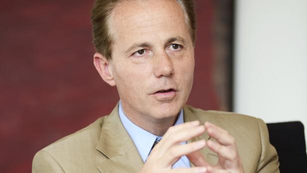 Ein Mann in einem hellbraunen Anzug gestikuliert mit seinen Händen.