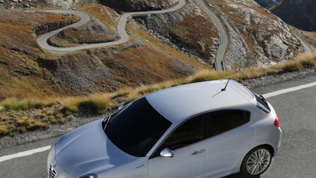 Ein silberner Alfa Romeo fährt auf einer Bergstraße mit Serpentinen.