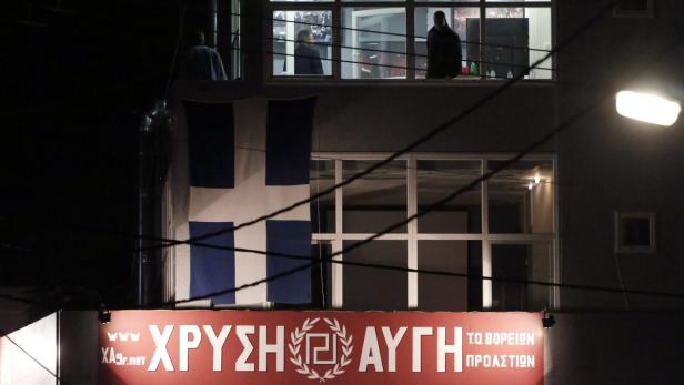 Ein Gebäude mit einer griechischen Flagge und einem Banner der „Chrysi Avgi“ bei Nacht.