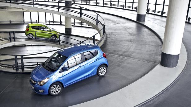 Ein blauer Kleinwagen fährt eine gewundene Rampe in einem Parkhaus hinauf.