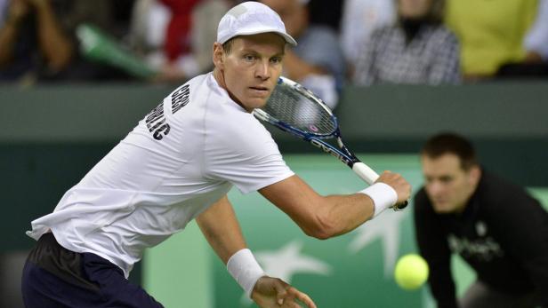 Ein Tennisspieler mit weißem Hemd und Kappe schlägt einen Ball.