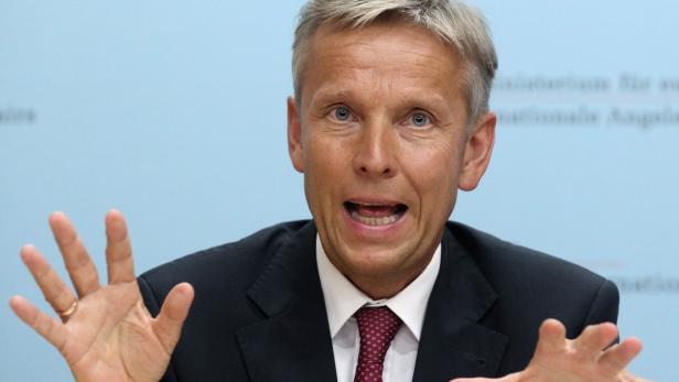 Ein Mann im Anzug gestikuliert mit offenen Händen.