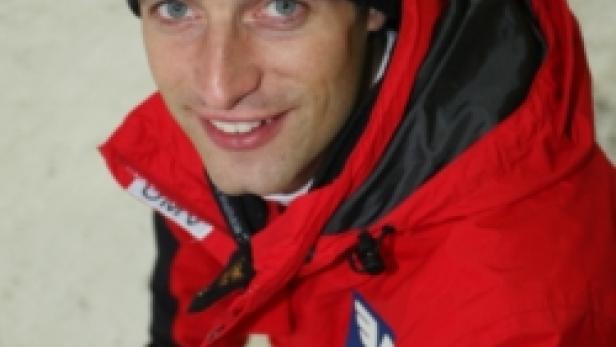 Ein lächelnder Mann in Sportkleidung mit Sponsorenlogos.