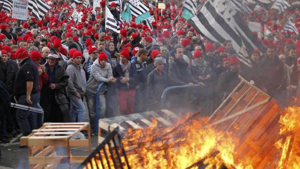 Eine Menschenmenge mit bretonischen Flaggen demonstriert vor einem brennenden Barrikade.