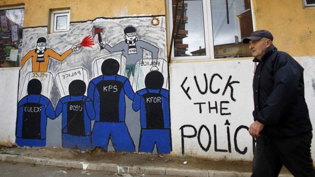 Ein Mann geht an einer Wand mit Graffiti vorbei, die Polizisten und Protestierende darstellen.