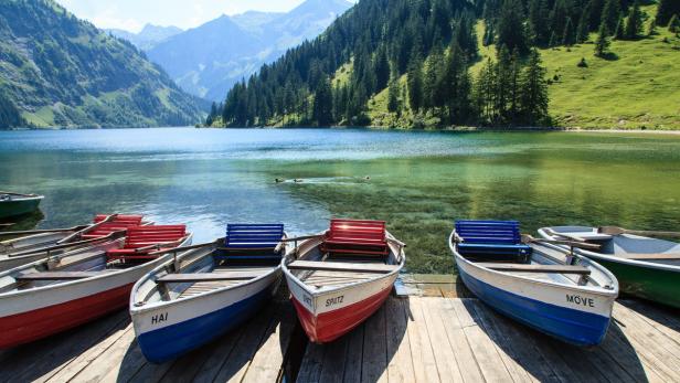 Mehrere Boote liegen an einem Holzsteg vor einem Bergsee.