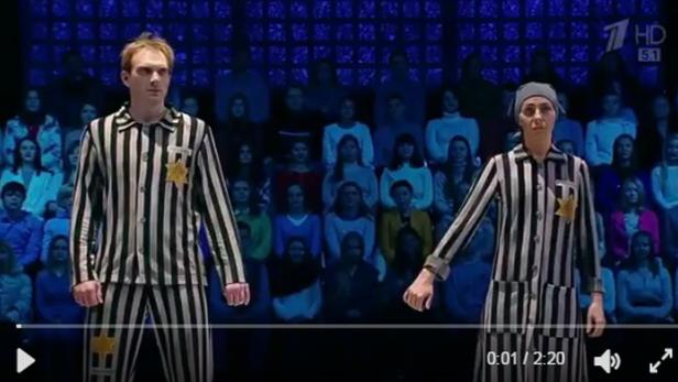 Zwei Personen in gestreiften Anzügen mit gelben Sternen stehen vor einem Publikum.