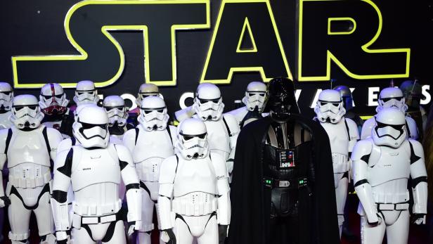 Eine Gruppe von Stormtroopern und Darth Vader stehen vor einem „Star Wars“-Logo.