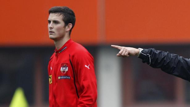 Ein junger Mann in roter Trainingsjacke der österreichischen Nationalmannschaft wird von einem Trainer angewiesen.