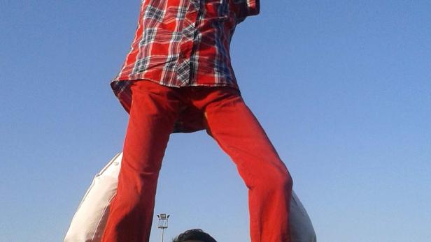 Ein Junge sitzt auf den Schultern eines Mannes vor einer Menschenmenge und bunten Flaggen.