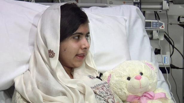 Malala Yousafzai liegt mit einem Teddybär im Krankenhausbett.