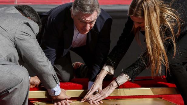 Robert De Niro hinterlässt seinen Handabdruck im Zement, zusammen mit zwei weiteren Personen.