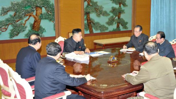 Kim Jong-un sitzt mit mehreren Beamten an einem Tisch.