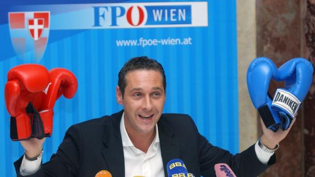 Ein Mann hält je einen roten und einen blauen Boxhandschuh in die Höhe; im Hintergrund ein FPÖ Wien Banner.