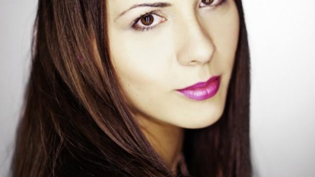 Porträt einer Frau mit langen, braunen Haaren und pinkfarbenem Lippenstift.