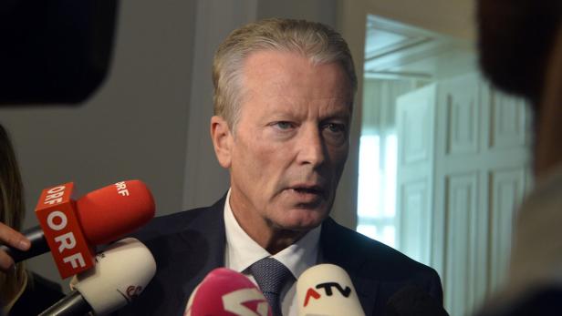 Ein Mann spricht in mehrere Mikrofone vor einem neutralen Hintergrund.