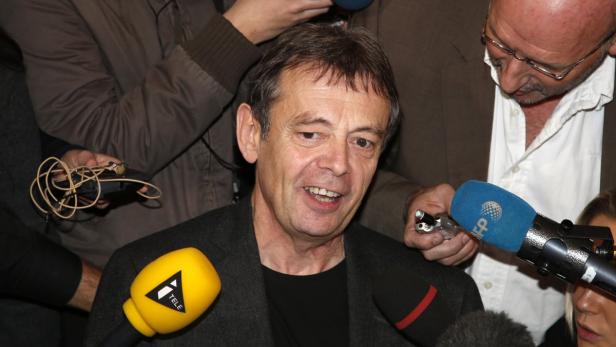 Ein Mann wird von Reportern mit Mikrofonen umringt.