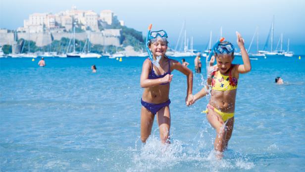 Zwei Mädchen mit Schnorchelbrillen rennen im Meer Hand in Hand.