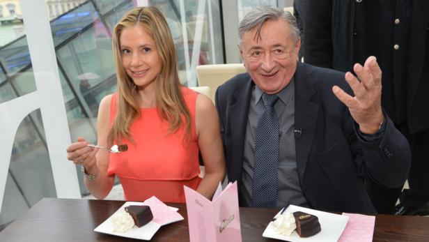 Eine Frau und ein Mann sitzen an einem Tisch mit Sachertorte und Sahne.