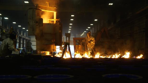 Ein Arbeiter in Schutzkleidung gießt flüssiges Metall in einer Gießerei.