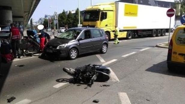 Ein Motorrad liegt nach einem Unfall auf der Straße, während Rettungskräfte helfen.