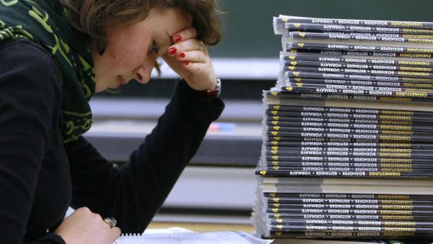 Eine erschöpfte Studentin sitzt neben einem Stapel „Chemiestunde“-Büchern.