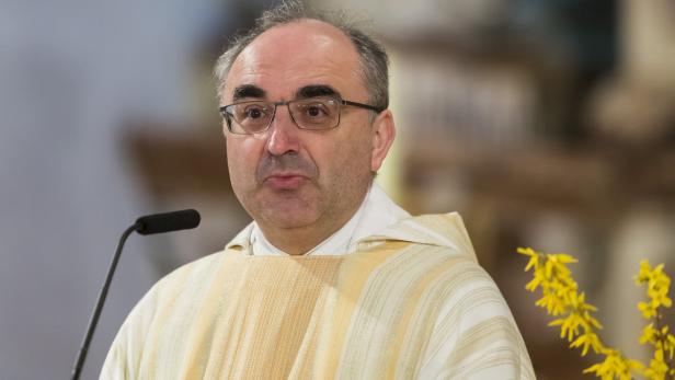 Ein Priester mit Brille steht an einem Mikrofon.