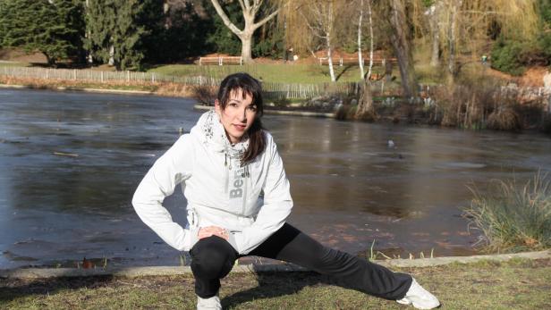 Eine Frau dehnt sich an einem teilweise gefrorenen See in einem Park.
