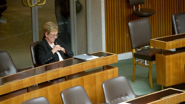 Eine Frau sitzt an einem Tisch in einem Konferenzraum und blickt nach unten.