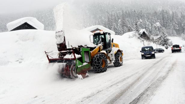 Eine Schneefräse räumt eine verschneite Straße, während Autos vorbeifahren.