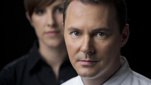 Ein Mann im Vordergrund, mit einer Frau unscharf im Hintergrund.